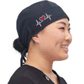 Ashtown Clothing black medical scrub hat with a white heartbeat and red heart embroidery worn by a smiling nurse
