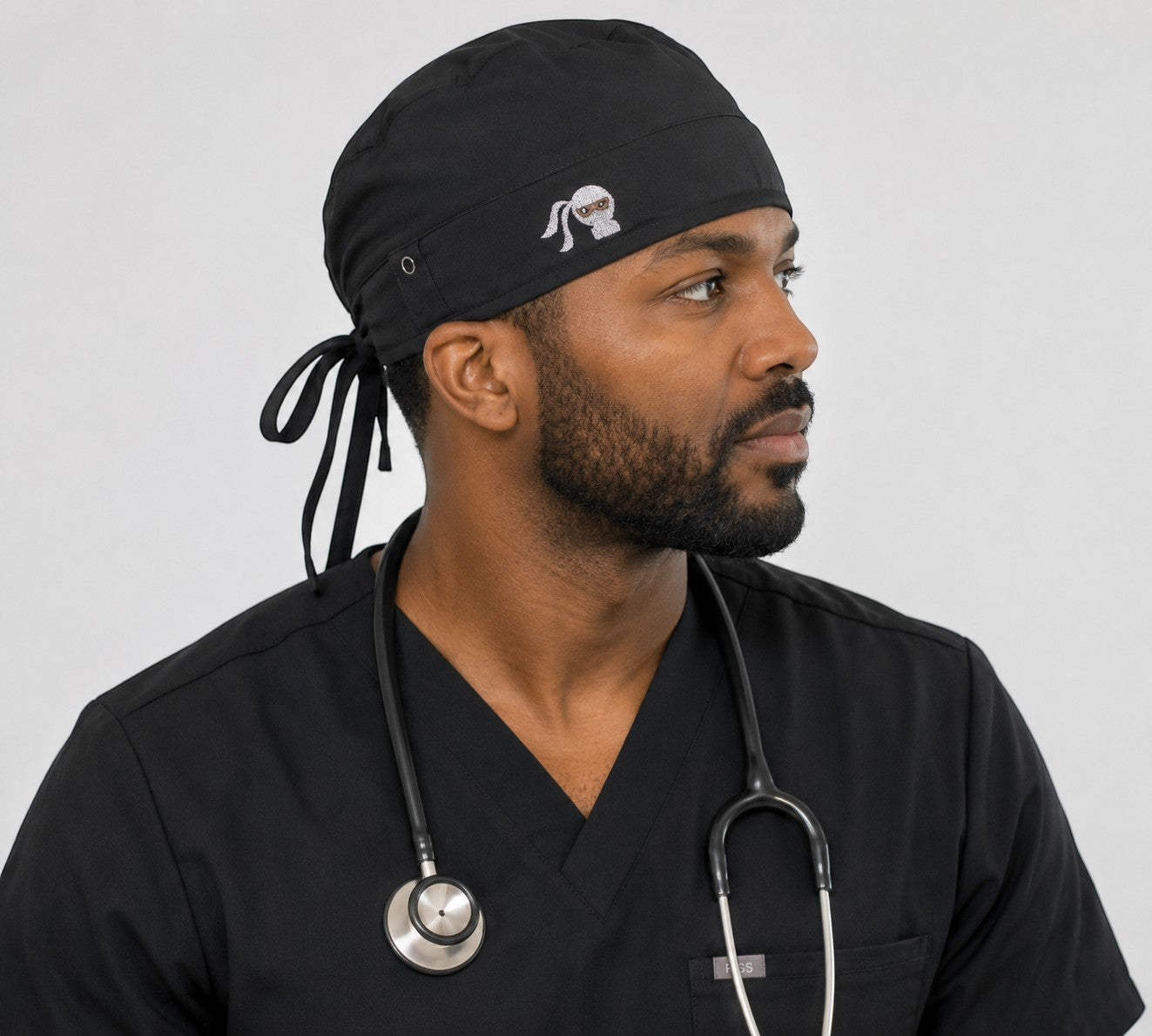 Ashtown Clothing black medical scrub hat with tie-back closure worn by a male healthcare professional