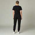 Back view of a model wearing Ashtown Clothing black petite performance jogger scrub pants with ribbed ankle cuffs.