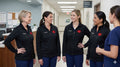 Ashtown Clothing women's black performance full zip medical jackets with custom embroidery in a hospital hallway.